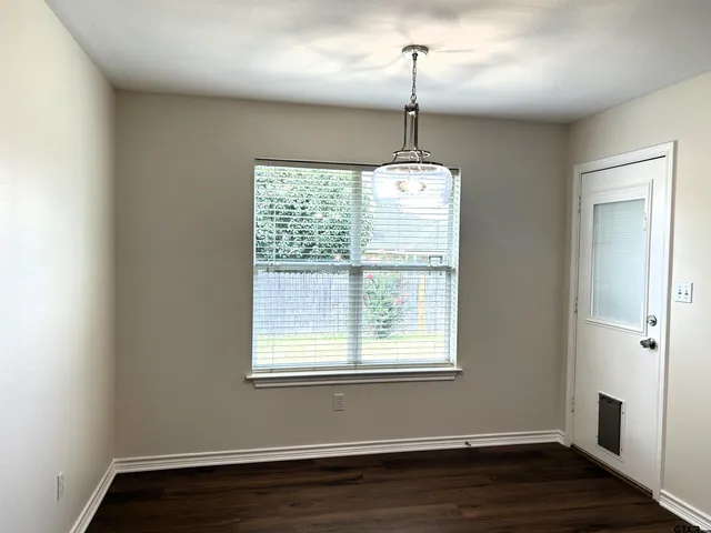 a view of an empty room with wooden floor fridge and a window