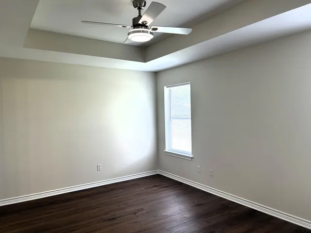 an empty room with wooden floor ceiling fan and window