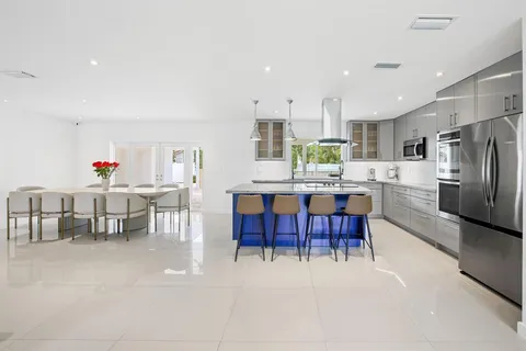 a kitchen with stainless steel appliances kitchen island granite countertop a dining table chairs and a refrigerator