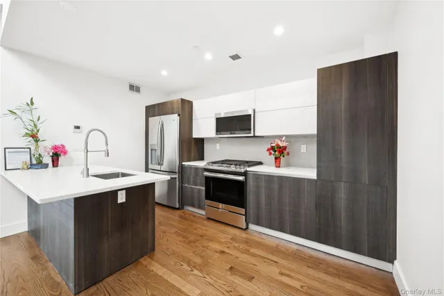 a kitchen with stainless steel appliances a sink dishwasher a refrigerator and a stove with wooden floor