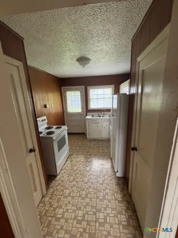 a view of a refrigerator in kitchen and an empty room
