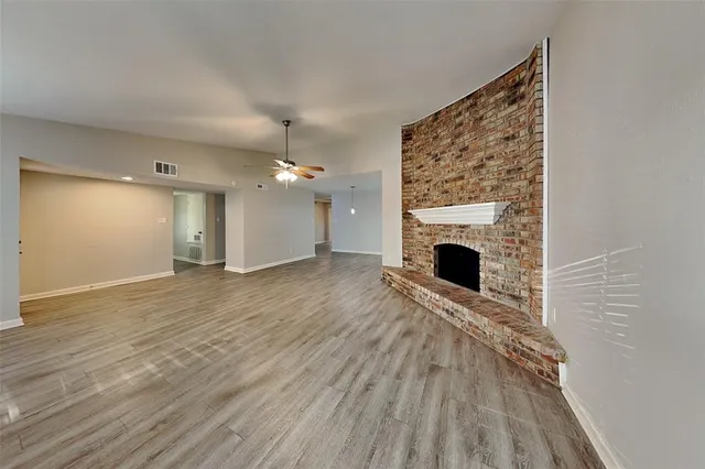 a view of an empty room with wooden floor fireplace and a window