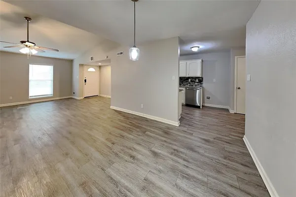 a view of an empty room with wooden floor and kitchen view