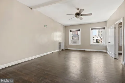 an empty room with wooden floor chandelier fan and windows