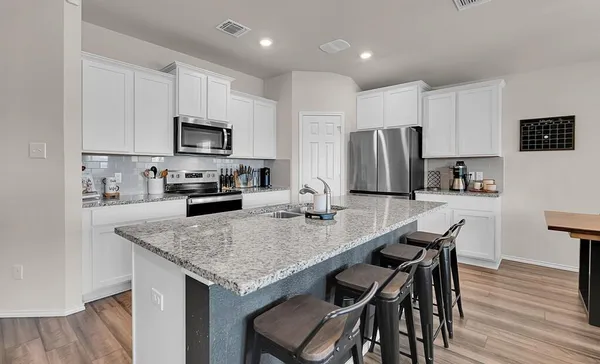 a kitchen with kitchen island granite countertop a table chairs microwave and refrigerator