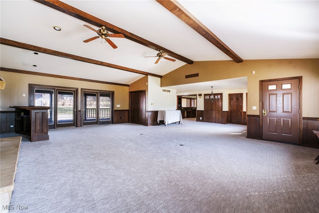 7059 Stewart Sharon Road Hubbard, OH 44425 - Photo 9 of 49 Unfurnished living room featuring a wainscoted wall, visible vents, a ceiling fan, wood walls, and vaulted ceiling with beams
