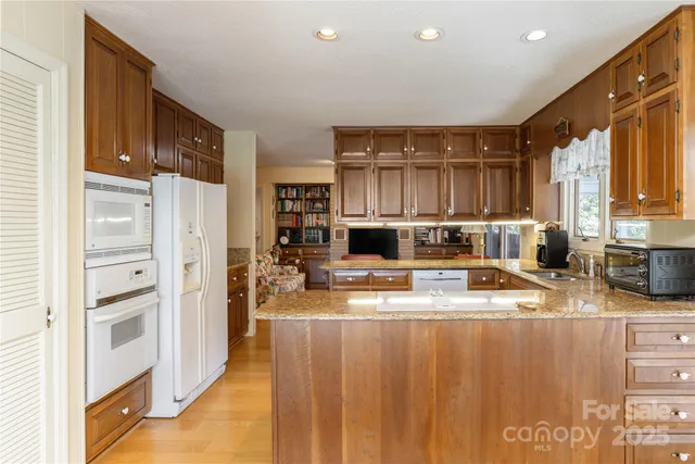 a kitchen with stainless steel appliances granite countertop a refrigerator a stove a sink and white cabinets with wooden floor