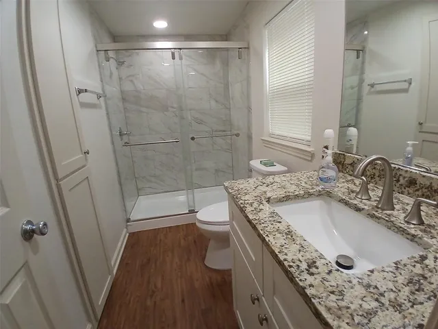 a bathroom with a granite countertop sink a toilet a mirror and shower