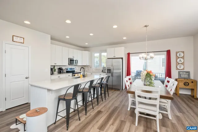 a kitchen with stainless steel appliances kitchen island granite countertop a dining table chairs and white cabinets