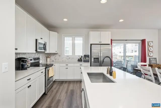 a large white kitchen with granite countertop a sink a counter space appliances and cabinets