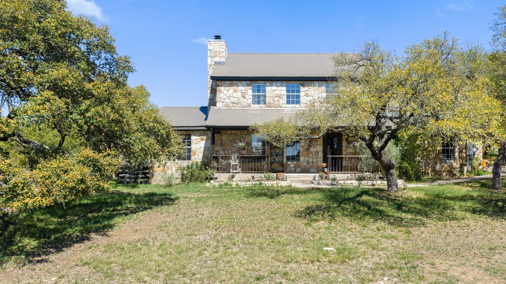 290 Sunset Ridge Dripping Springs, TX 78620 - Photo 36 of 39 Rear view of property featuring stone siding, a metal roof, covered porch, a lawn, and a chimney