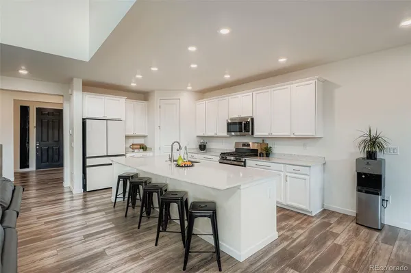 a kitchen with stainless steel appliances a microwave a stove a sink a refrigerator and white cabinets with wooden floor