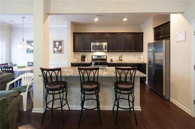a kitchen with stainless steel appliances a dining table chairs refrigerator and microwave