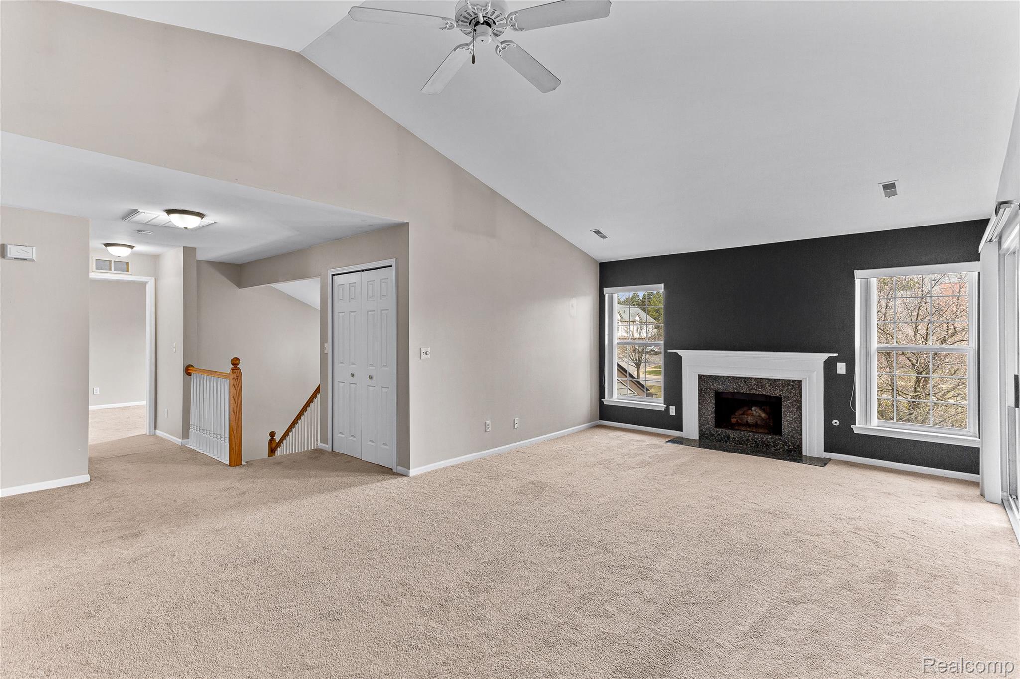 3553 Oakmonte Boulevard Rochester, MI 48306 - Photo 2 of 42 Vaulted ceiling living space featuring a fireplace with a dark stone surround and white mantel, dual windows, and light-toned carpet