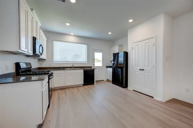 a kitchen with stainless steel appliances granite countertop a refrigerator a sink dishwasher a stove and white cabinets with wooden floor