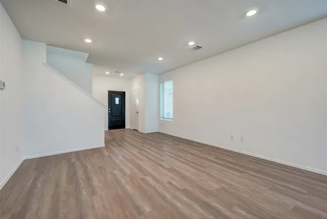 a view of an empty room with wooden floor and kitchen space