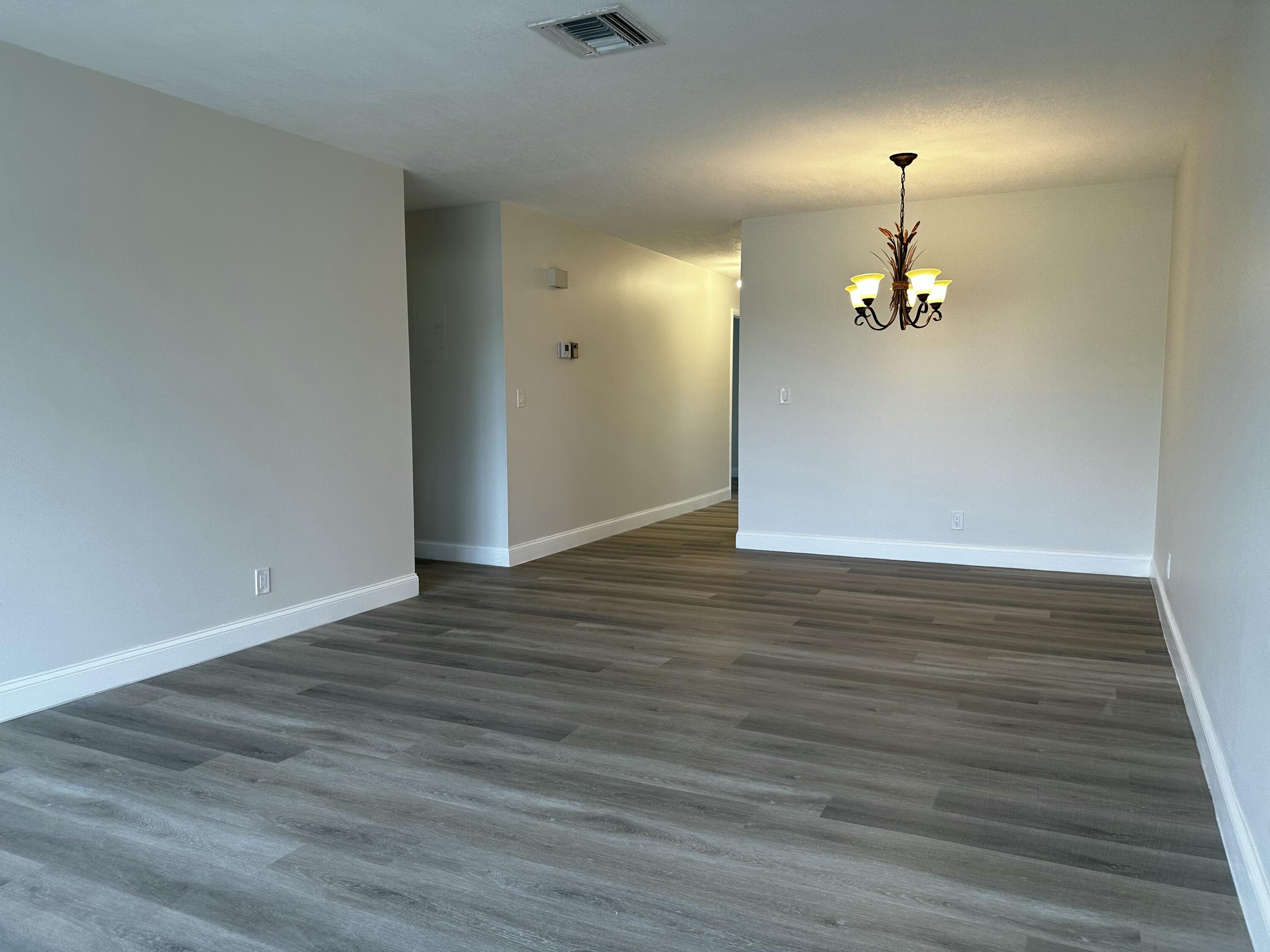 13682 Vía Flora, Unit H Delray Beach, FL 33484 - Photo 16 of 28 an empty room with wooden floor chandelier and windows