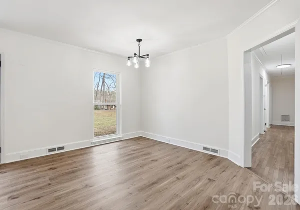 an empty room with wooden floor chandelier fan and windows