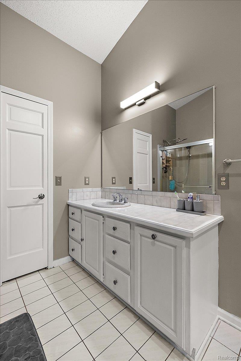 707 West Sutton Road Metamora, MI 48455 - Photo 45 of 84 Vaulted ceiling with a contemporary vanity light fixture, white vanity with ample storage, integrated sink, and a tiled shower enclosure