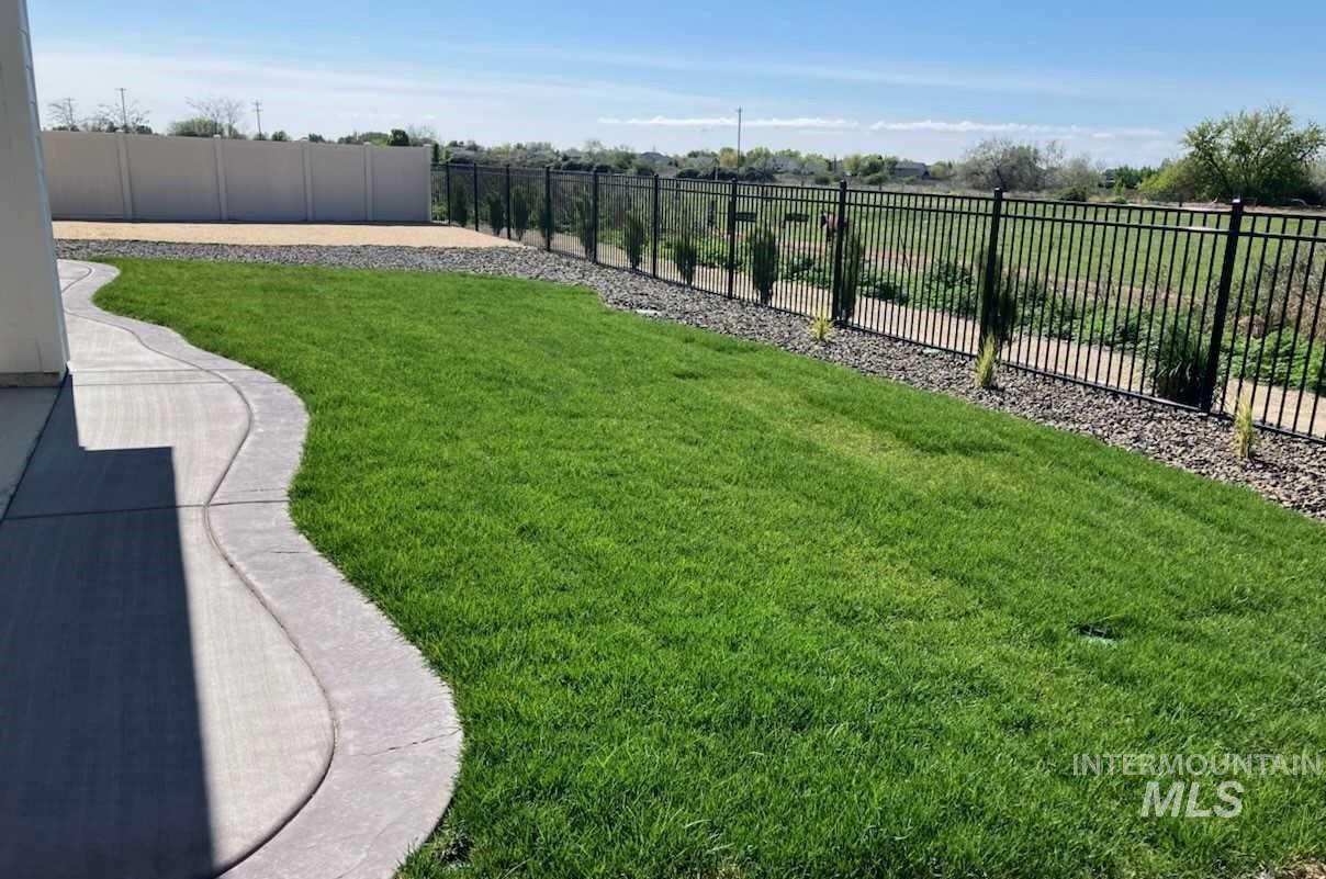 12557 West Wayfaring Drive Star, ID 83669 - Photo 5 of 25 Expansive green lawn featuring a curvilinear concrete pathway, black metal fencing, and decorative gravel landscaping with planted shrubs