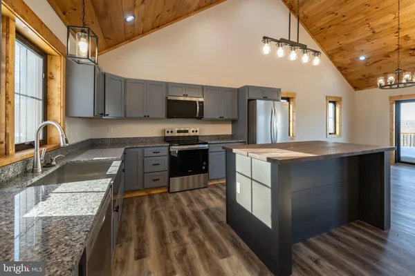 a kitchen with stainless steel appliances granite countertop a refrigerator a sink dishwasher a stove and white countertops with wooden floor