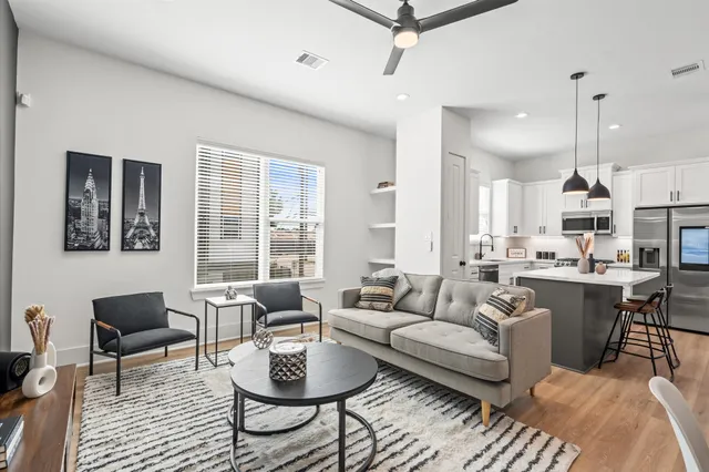 a living room with furniture a rug kitchen view and a large window