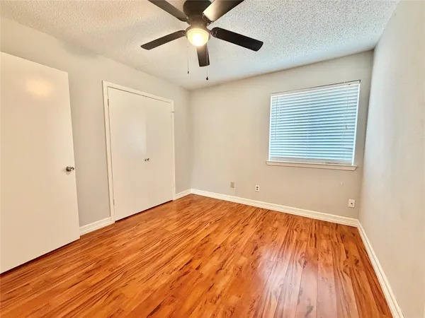 a view of an empty room with wooden floor and a ceiling fan