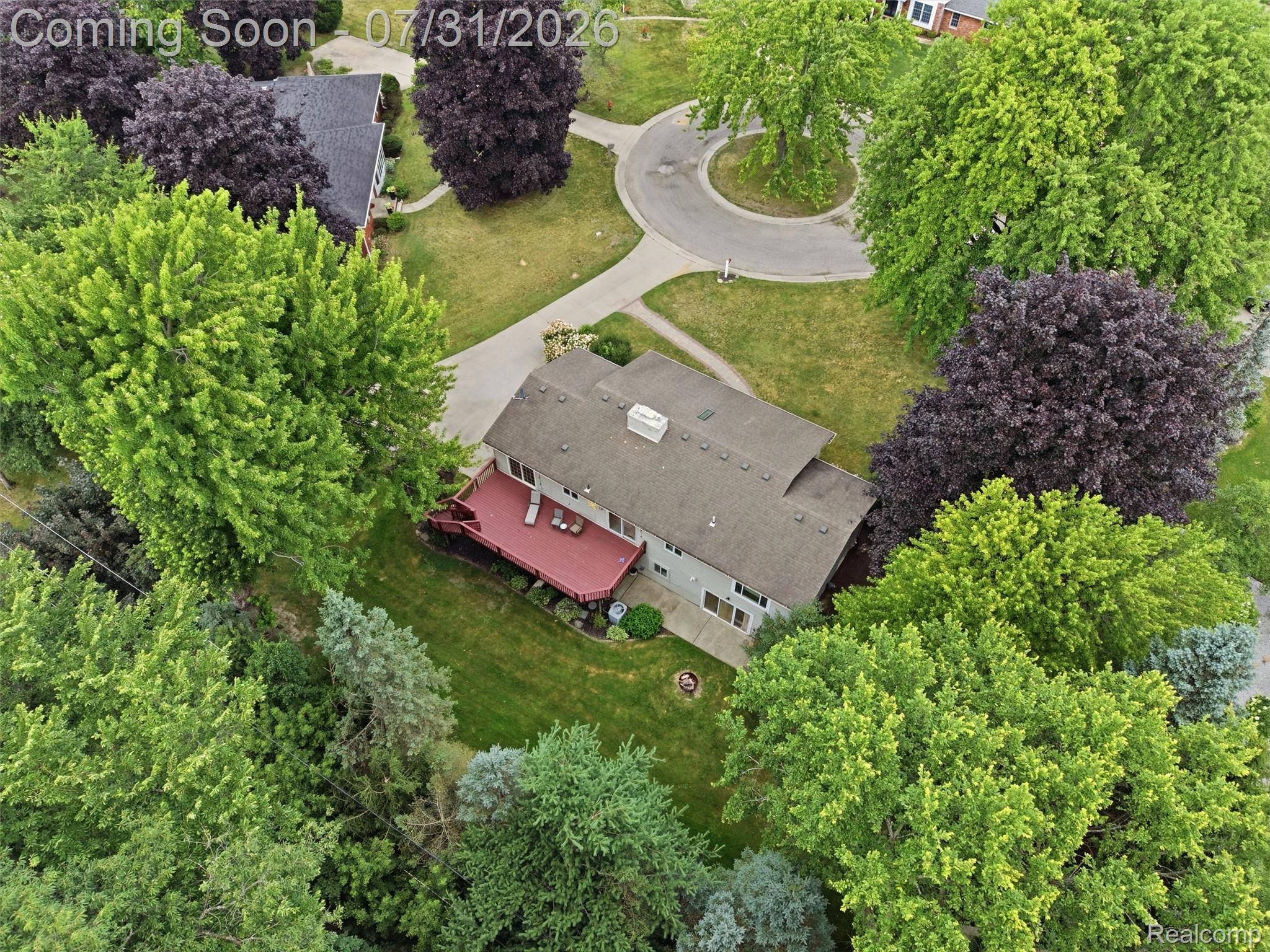 138 Aintree Road Rochester, MI 48306 - Photo 11 of 53 Aerial perspective showcasing a property surrounded by mature trees, featuring a red-stained wooden deck, a green lawn area, and a grey asphalt shingle roof