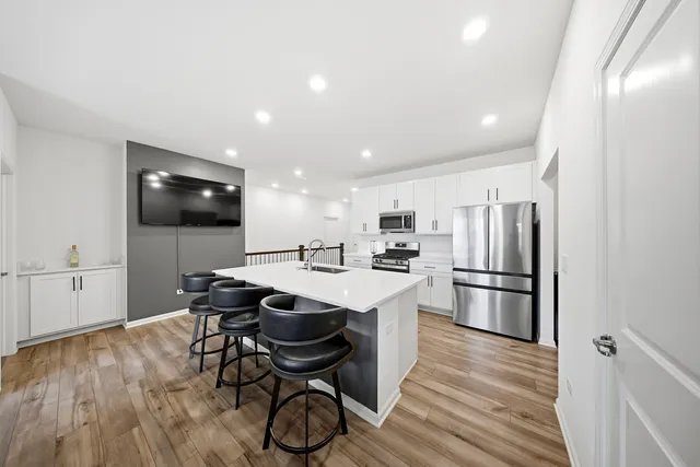 a kitchen with stainless steel appliances a microwave a stove a refrigerator and a dining table with wooden floor