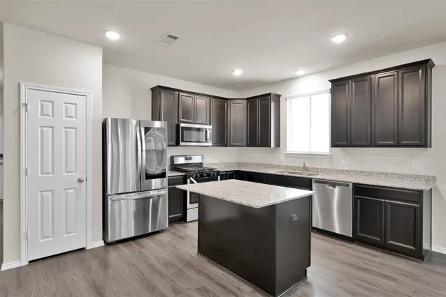 a kitchen with stainless steel appliances granite countertop a refrigerator a sink dishwasher a stove and white countertops with wooden floor