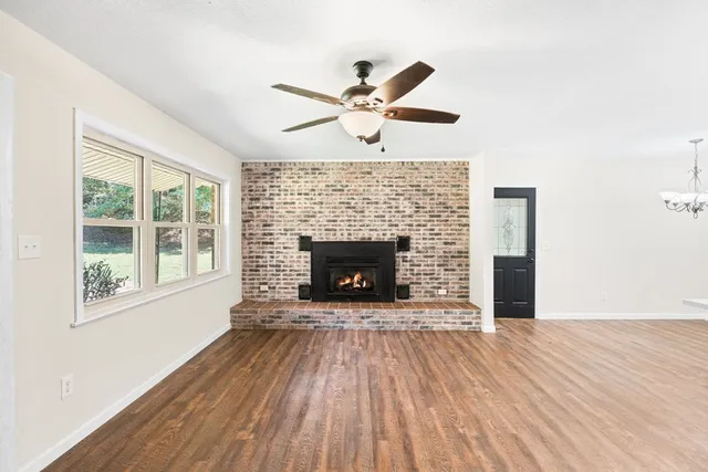 a view of a livingroom with a fireplace a ceiling fan and wooden floor