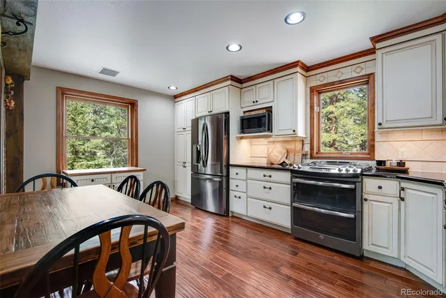 a kitchen with stainless steel appliances granite countertop a stove a refrigerator a sink dishwasher a dining table and chairs with wooden floor