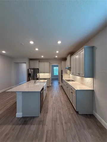 a large kitchen with stainless steel appliances a large counter top a wooden floors and a large window