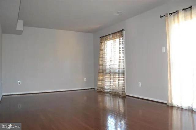 an empty room with wooden floor and windows with curtains