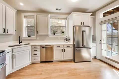 a kitchen with stainless steel appliances a sink dishwasher a stove top oven a refrigerator with wooden floor and cabinets