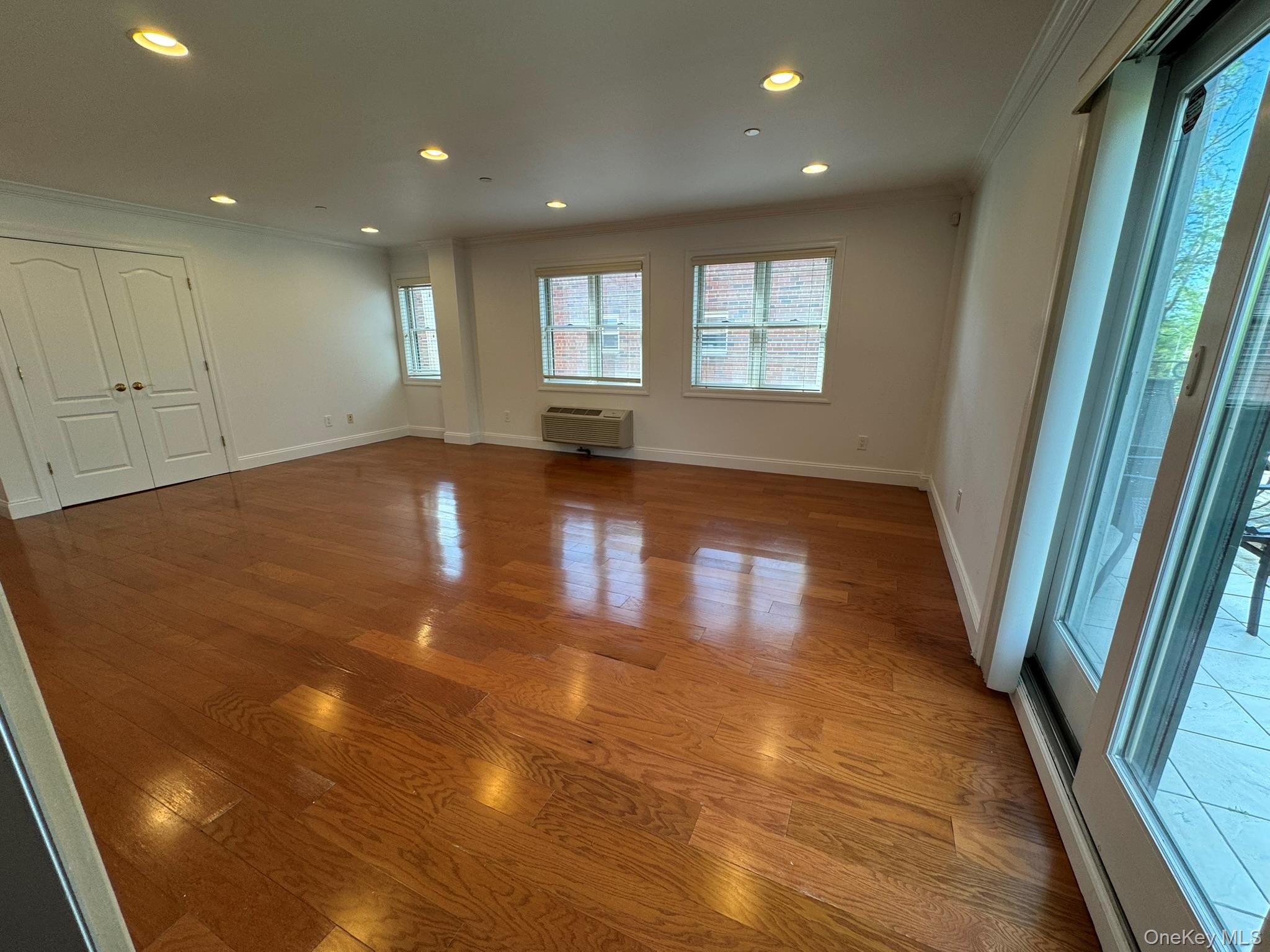 42-23 212th Street, Unit 3C Queens, NY 11361 - Photo 2 of 13 Unfurnished room with ornamental molding, recessed lighting, wood finished floors, baseboards, and a wall unit AC