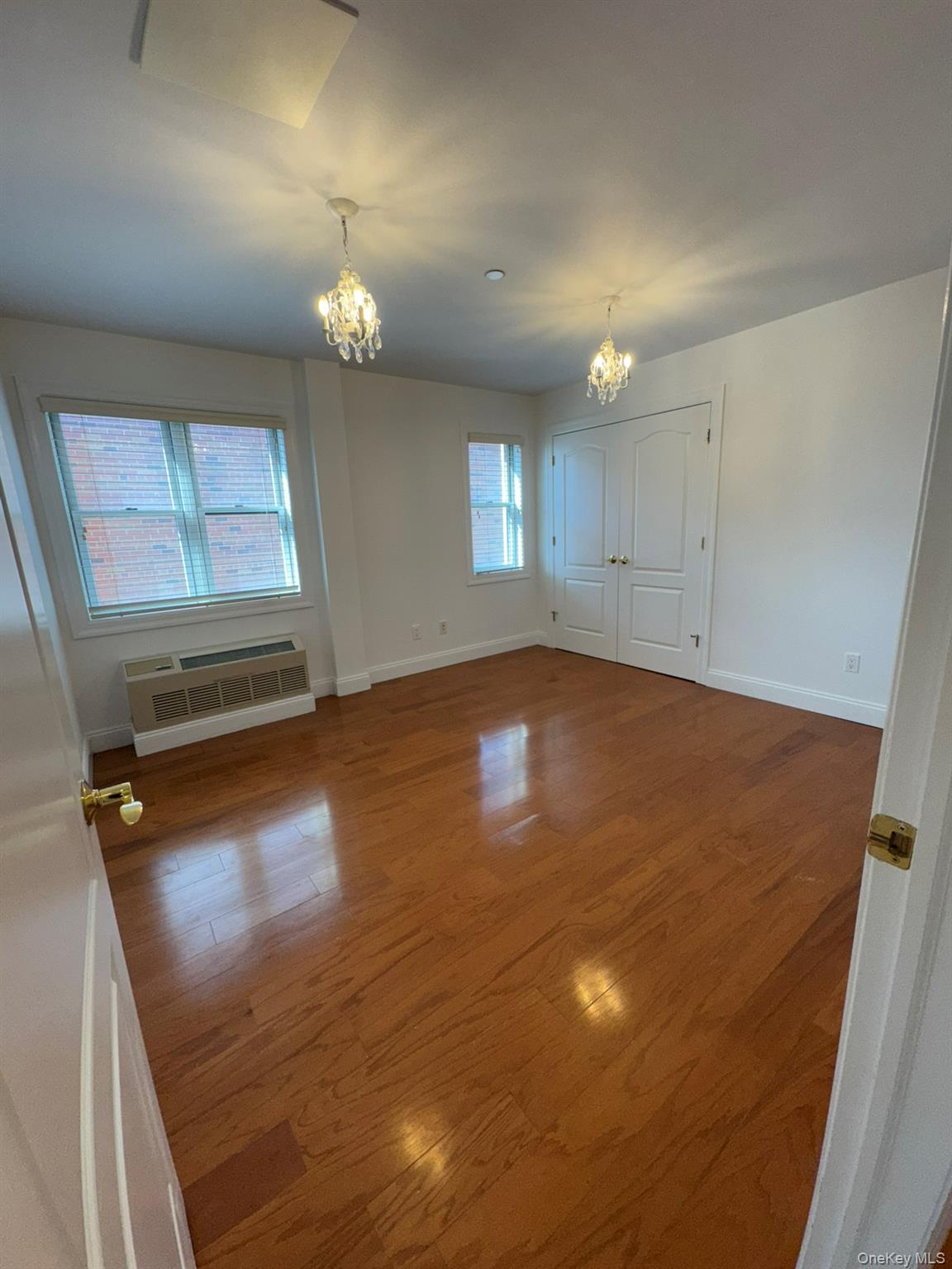42-23 212th Street, Unit 3C Queens, NY 11361 - Photo 4 of 13 Empty room featuring a chandelier, a wall mounted AC, baseboards, and wood finished floors