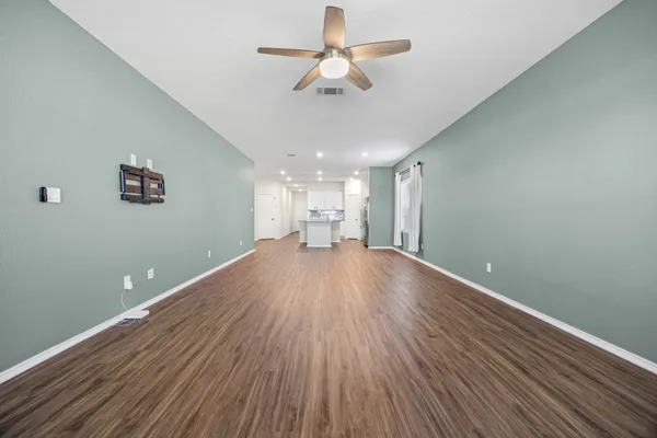 an empty room with wooden floor chandelier fan and windows