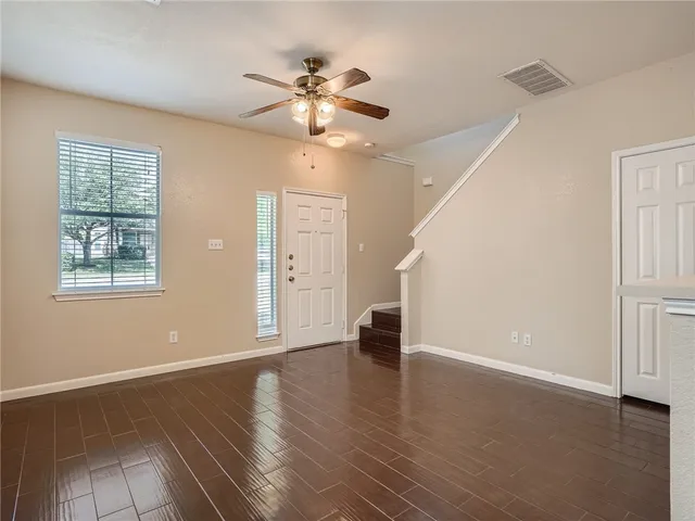 an empty room with wooden floor chandelier fan and windows