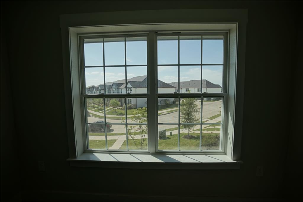1764 Palladio Loop Princeton, TX 75407 - Photo 39 of 40 Double-hung window with a grid pattern, white trim, and a sill, offering a view of a residential street with sidewalks and landscaping