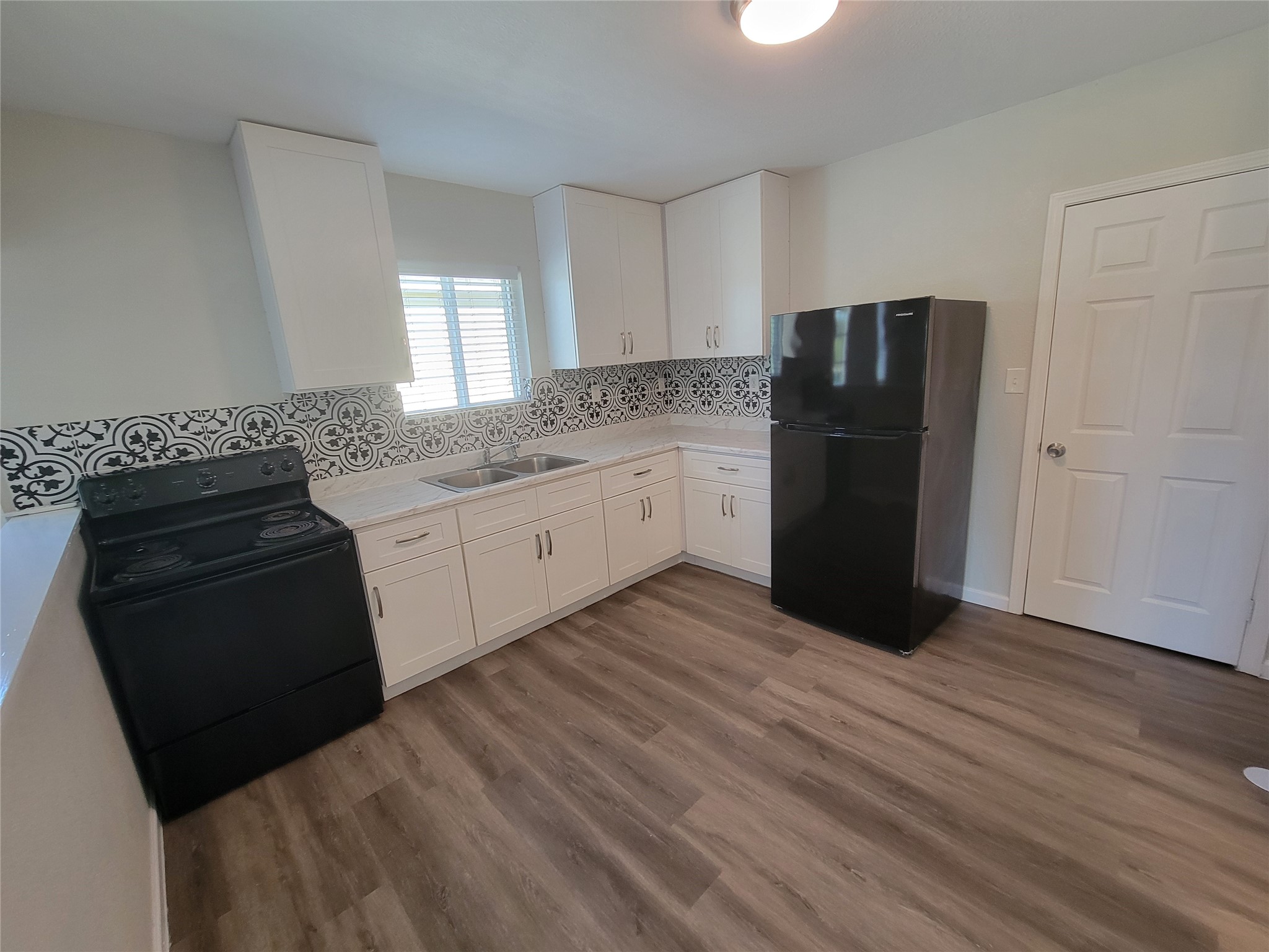 715 11th Street, Unit A Dickinson, TX 77539 - Photo 3 of 14 This kitchen features modern white cabinetry with stylish black and white patterned backsplash. It includes sleek black appliances, a spacious countertop, and wood-style flooring, creating a clean and inviting space.
