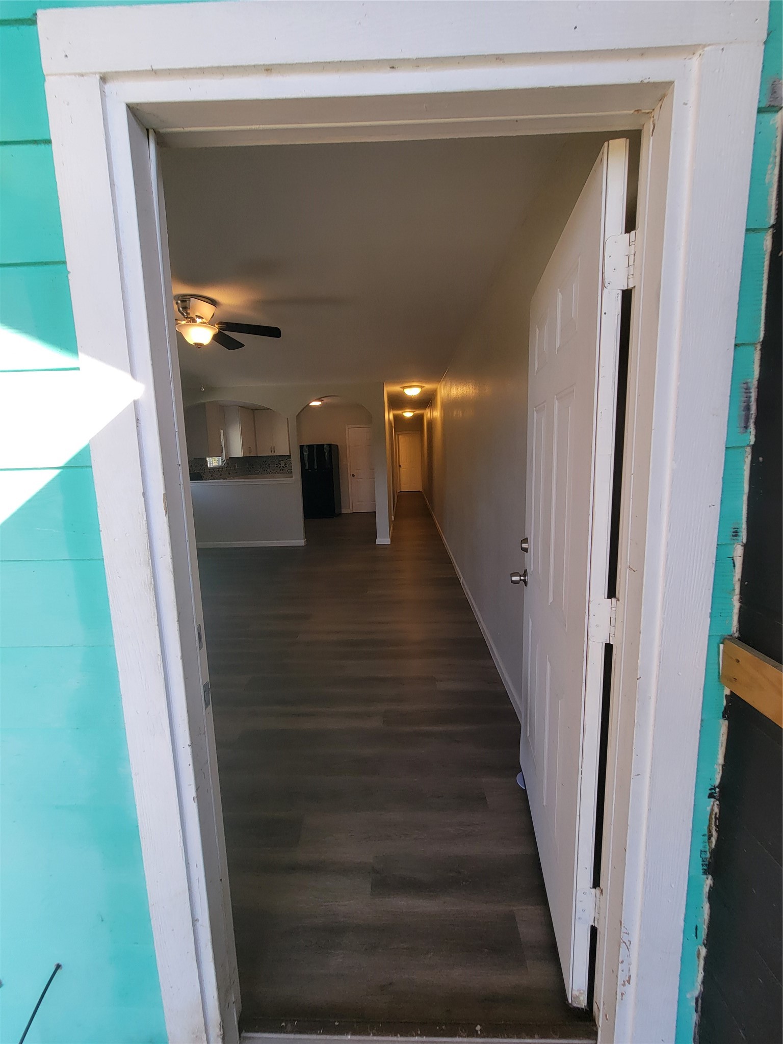 715 11th Street, Unit A Dickinson, TX 77539 - Photo 10 of 14 This photo shows the entrance to Unit A (left side) with a partially open door revealing a hallway with wood-style flooring. Visible is a ceiling fan in the living area and a glimpse of the kitchen with a modern backsplash. The space is bright with an inviting layout.
