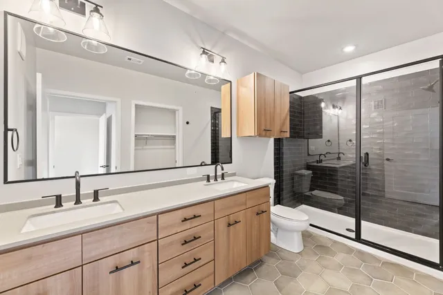 a spacious bathroom with double sink a toilet a mirror and shower