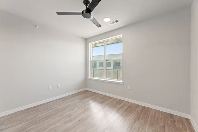 an empty room with wooden floor fan and windows