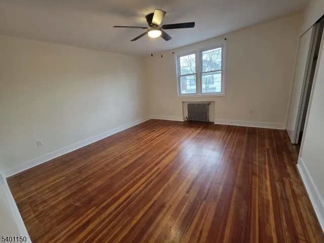 an empty room with wooden floor ceiling fan and windows