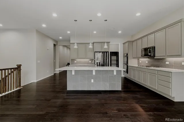 a large kitchen with stainless steel appliances a large counter top a stove a sink dishwasher a refrigerator and white cabinets with wooden floor