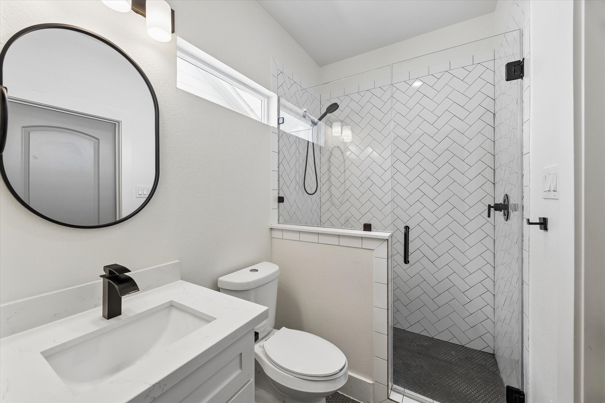 2749 Redrock Street, Unit B Houston, TX 77088 - Photo 16 of 24 The private primary bath includes Shaker-style cabinetry supporting a quartz counter top highlighted by a framed mirror mounting on the wall with lighting above. The gorgeous walk-in shower has a herringbone patterned tile.