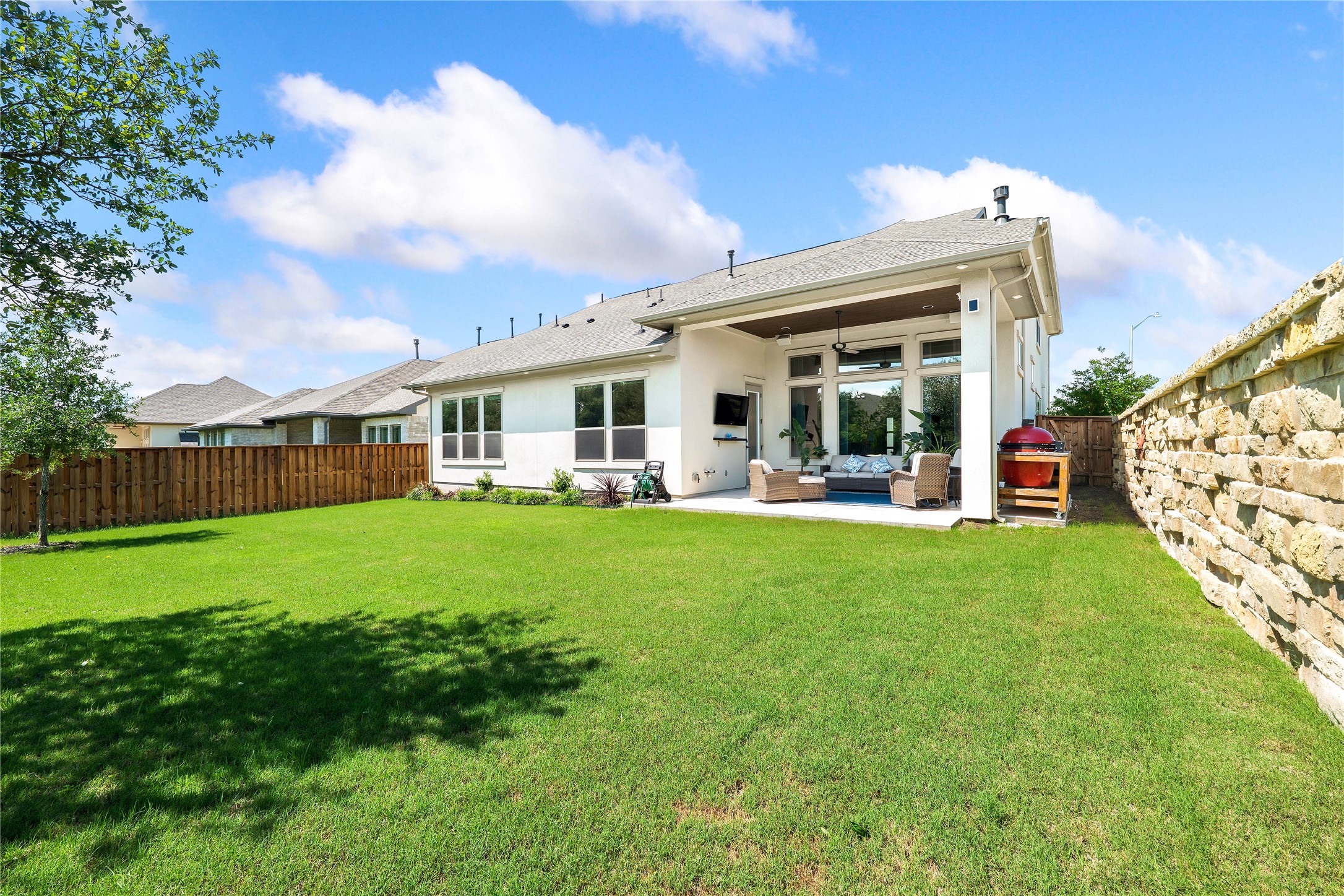2408 Nate's Place Georgetown, TX 78633 - Photo 2 of 40 View of spacious backyard with vibrant green grass, a stone retaining wall, and a covered patio ideal for outdoor relaxation.
