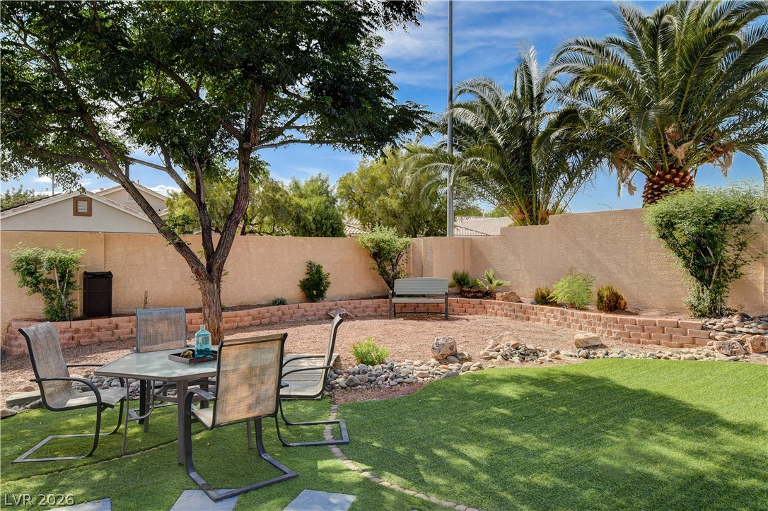 910 Cobblestone Cove Road North Las Vegas, NV 89081 - Photo 23 of 30 A private backyard oasis features artificial turf, a rock garden, and a shade tree, perfect for outdoor enjoyment.