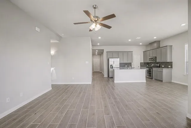 a view of an empty room with wooden floor and a kitchen
